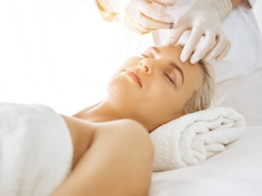 Güzellik uzmanı elleri güneşli klinikte kadın yüzüne şırınga ile güzellik prosedürü uyguluyor. Kozmetik tıp ve cerrahi, güzellik enjeksiyonları konsepti