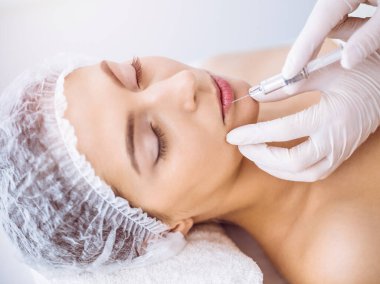 Güzellik uzmanı güneşli spa merkezinde genç esmer bir kadının yüzüne şırıngayla güzellik prosedürü uyguluyor. Kozmetik ilaç ve ameliyat, güzellik iğneleri.