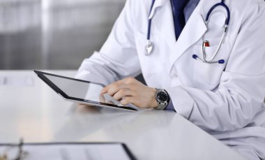 Bilinmeyen erkek doktor klinikteki tablet bilgisayarla yakın planda çalışıyor. İşteki genç doktor. Mükemmel sağlık hizmeti, tıp konsepti