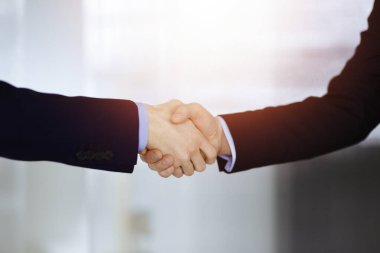 İş adamları el sıkışıyor, yakın plan. Güneşli bir modern ofiste duran bir grup tanınmamış iş adamı. Takım çalışması, ortaklık ve el sıkışma kavramı