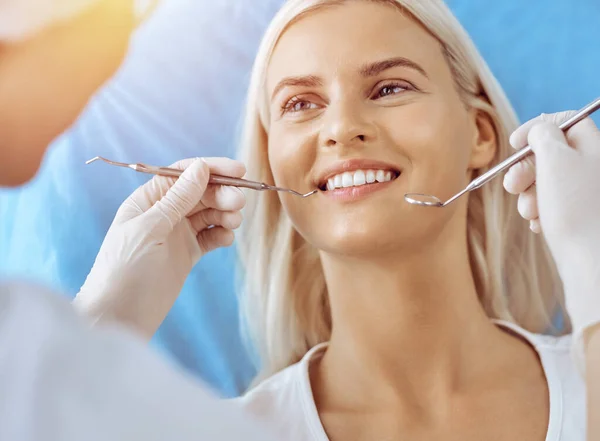 Lachende blonde vrouw onderzocht door tandarts in zonnige tandheelkundige kliniek. Gezonde tanden en geneeskundeconcept — Stockfoto