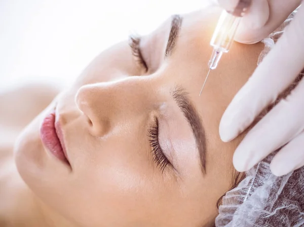 Beautician doing beauty procedure with syringe to face of young brunette woman in sunny spa center. Cosmetic medicine and surgery, beauty injections