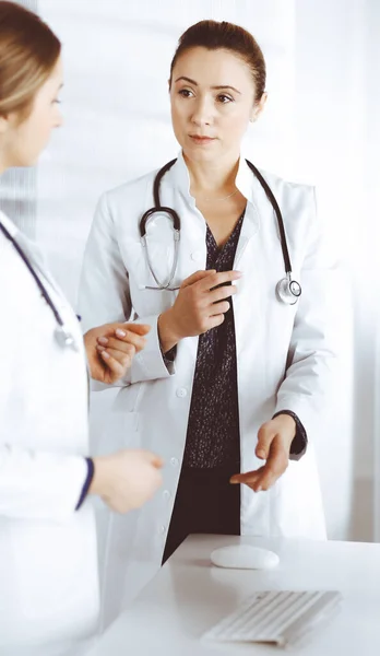 Duas médicas estão discutindo terapia médica, enquanto estão na mesa em um consultório da clínica. Os médicos usam o computador pc no trabalho. Trabalho em equipe em medicina — Fotografia de Stock