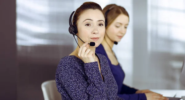 Deux femmes d'affaires ont des conversations avec les clients par écouteurs, tout en étant assis au bureau dans un bureau moderne. Groupe de personnes diverses dans un centre d'appels. Télémarketing et service à la clientèle — Photo