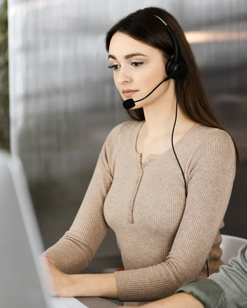 Deux jeunes dans des casques d'écoute parlent aux clients, assis au bureau dans un bureau moderne. Concentre-toi sur la femme. Opérateurs de centre d'appels au travail — Photo