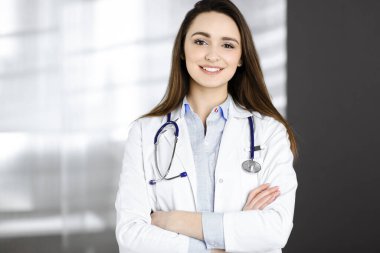 Neşeli gülümseyen kadın doktor klinikte kollarını kavuşturmuş duruyor. İş yerindeki dost canlısı bir doktorun portresi. Hastanede mükemmel bir tıbbi hizmet. Tıp konsepti