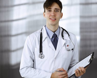 Modern klinikte dostane genç bir erkek doktor elinde bir panoyla dikiliyor. Tıp konsepti