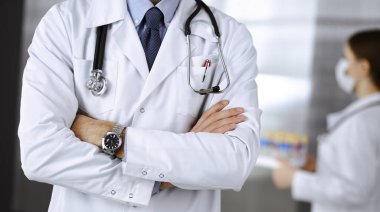 Koruyucu maskeli kimliği belirsiz erkek doktor klinikte kollarını kavuşturmuş duruyor. Coronavirus salgını sırasında ilaç konsepti. Covid 2019