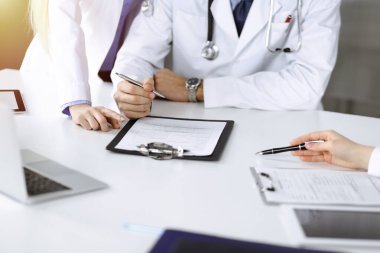 Bilinmeyen bir grup doktor masanın başında oturmuş güneşli hastane ofisinde hastalıkların tedavisini tartışıyorlar. Covid 2019