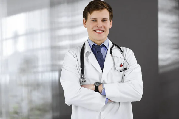 Un jeune médecin joyeux se tient debout les bras croisés dans une clinique. Portrait du médecin professionnel au travail. Concept de médecine — Photo