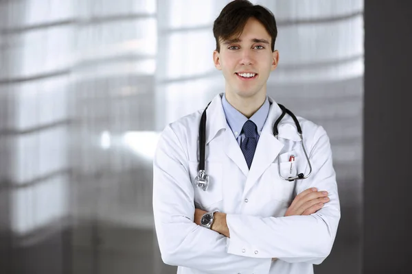 Vrolijke glimlachende man-dokter met gekruiste armen in de kliniek. Perfecte medische service met jonge slimme arts in het ziekenhuis. Geneesmiddelenconcept — Stockfoto