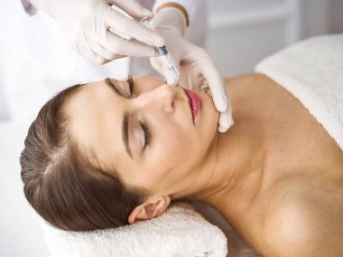 Güzellik uzmanı güneşli spa merkezinde genç esmer bir kadının yüzüne şırıngayla güzellik prosedürü uyguluyor. Kozmetik ilaç ve ameliyat, güzellik iğneleri.