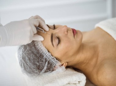 Güzellik uzmanı güneşli spa merkezinde genç esmer bir kadının yüzüne şırıngayla güzellik prosedürü uyguluyor. Kozmetik ilaç ve ameliyat, güzellik iğneleri.
