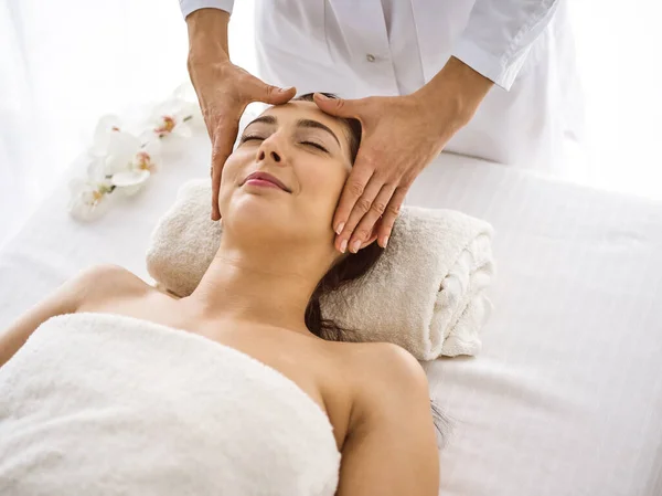 Красива брюнетка жінка насолоджується масажем обличчя комфортно і бісфол. Розслаблююче лікування в медицині та концепціях спа-центру — стокове фото