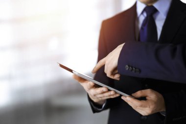 İş adamları yeni projelerini tartışmak için bir tablet bilgisayar kullanıyorlar, güneşli modern ofiste duruyorlar. İş yerinde iş arkadaşı olan tanınmamış bir işadamı ya da erkek girişimci