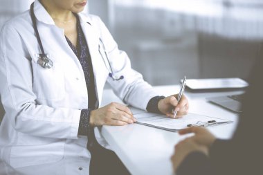 Bilinmeyen kadın-doktor, bir klinikteki dolapta birlikte otururken hastasına bazı tıbbi tavsiyeler yazıyor. Hekim bir dosya kullanıyor, yakın plan. Mükemmel.