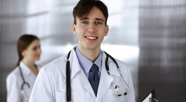 Modern klinikte dostane genç bir erkek doktor elinde bir panoyla dikiliyor. Bayan meslektaşım, doktorların arka planında ilaç kayıtları doldurmakla meşgul. Tıp konsepti