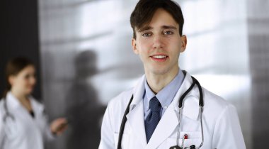 Modern klinikte dostane genç bir erkek doktor elinde bir panoyla dikiliyor. Bayan meslektaşım, doktorların arka planında ilaç kayıtları doldurmakla meşgul. Tıp konsepti