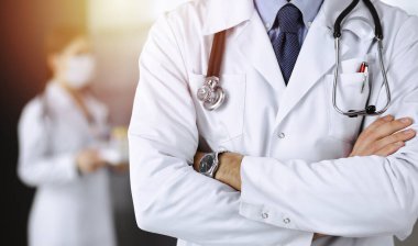 Güneşli klinikte kolları çapraz duran koruyucu maskeli kimliği belirsiz erkek doktor. Coronavirüs salgını sırasında ilaç kavramı