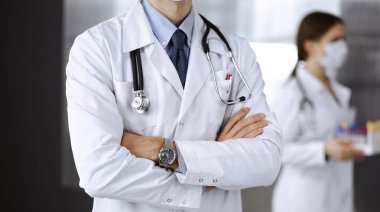 Koruyucu maskeli kimliği belirsiz erkek doktor klinikte kollarını kavuşturmuş duruyor. Coronavirus salgını sırasında ilaç konsepti. Covid 2019