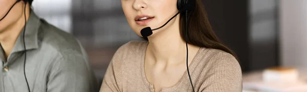 Dos jóvenes con auriculares están hablando con los clientes, mientras están sentados en el escritorio de una oficina. Concéntrate en mujer. Operadores de centros de llamadas en el trabajo —  Fotos de Stock