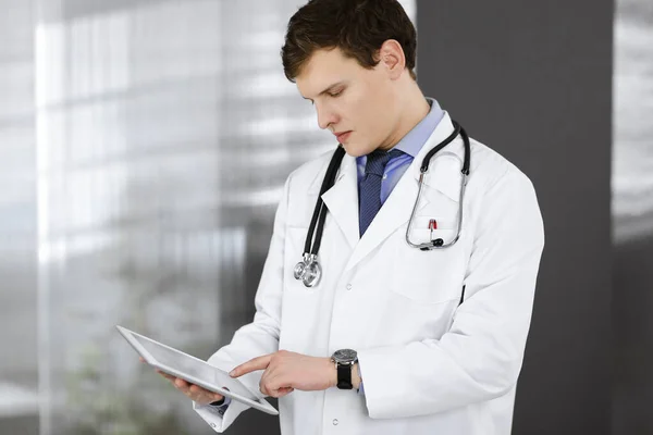 Mladý přátelský doktor kontroluje nějaké informace na svém počítači. Portrét profesionálního lékaře v práci na klinice. Koncept medicíny — Stock fotografie