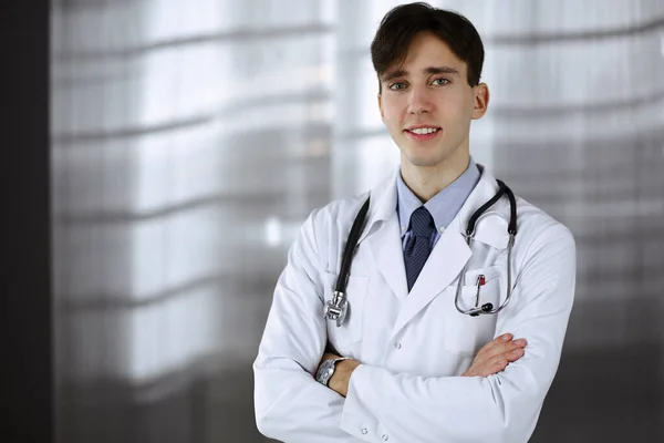 Veselý usměvavý lékař stojící se zkříženýma rukama na klinice. Perfektní lékařská služba s mladým chytrým lékařem v nemocnici. Koncept medicíny — Stock fotografie