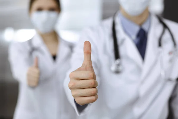 Unknown man-doctor and woman standing straight as a team and showing Ok sign with thumbs up in modern clinic. Medicine concept during Coronavirus pandemic. Covid 2019 — Stock Photo, Image