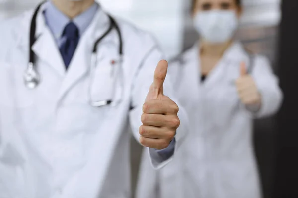 Unknown man-doctor and woman standing straight as a team and showing Ok sign with thumbs up in modern clinic. Medicine concept during Coronavirus pandemic. Covid 2019 — Stock Photo, Image