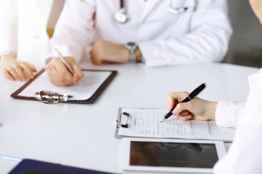 Bilinmeyen bir grup doktor masanın başında oturmuş güneşli hastane ofisinde hastalıkların tedavisini tartışıyorlar. Covid 2019