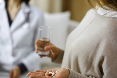Yakın plan kadın-hasta doktorunun yanında haplar tutuyor. İlaç alma, baş ağrısı veya ağrı kesici ilaçların tedavisi için zaman var. Coronavirus salgını ve kendini izolasyon süresince evde kal.