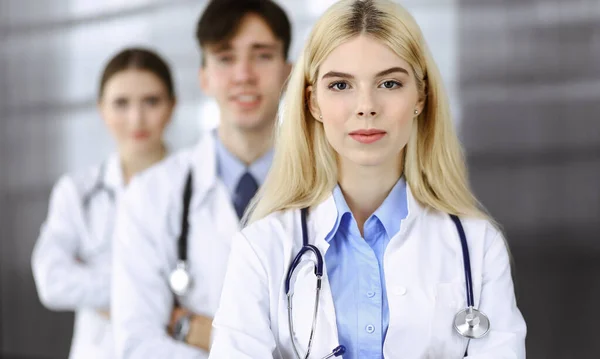 Gruppo di tre giovani medici in piedi come una squadra con le braccia incrociate in clinica moderna e pronto ad aiutare i pazienti. Concetto di medicina — Foto Stock