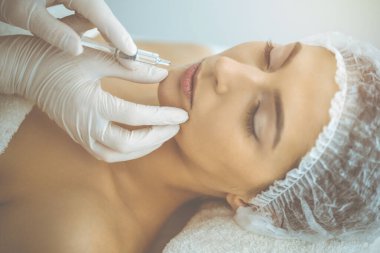 Güzellik uzmanı güneşli klinikte genç esmer kadının yüzüne şırıngayla güzellik prosedürü uyguluyor. Kozmetik ilaç ve ameliyat, güzellik iğneleri.