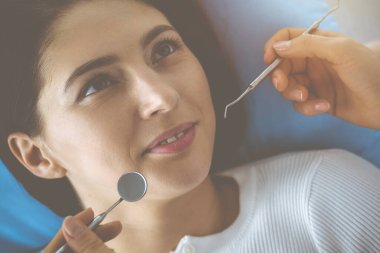 Gülümseyen esmer kadın diş hekimi tarafından muayene ediliyor. Hastanın ağzının yanında diş aletleri tutan bir doktorun elleri. Sağlıklı diş ve ilaç konsepti