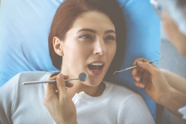 Gülümseyen esmer kadın diş hekimi tarafından muayene ediliyor. Hastanın ağzının yanında diş aletleri tutan bir doktorun elleri. Sağlıklı diş ve ilaç konsepti