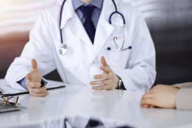 Bilinmeyen bir erkek doktor ve hasta kadın karanlık bir klinikte otururken bir şey tartışıyorlar, arka planda ışık parlıyor. Ellerin yakın çekimi