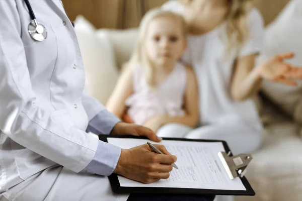 Dokter en patiënt. Kinderarts die klembord gebruikt terwijl ze het kleine meisje onderzoekt met haar moeder thuis. Ziek en ongelukkig kind bij medisch onderzoek. Geneesmiddelenconcept — Stockfoto