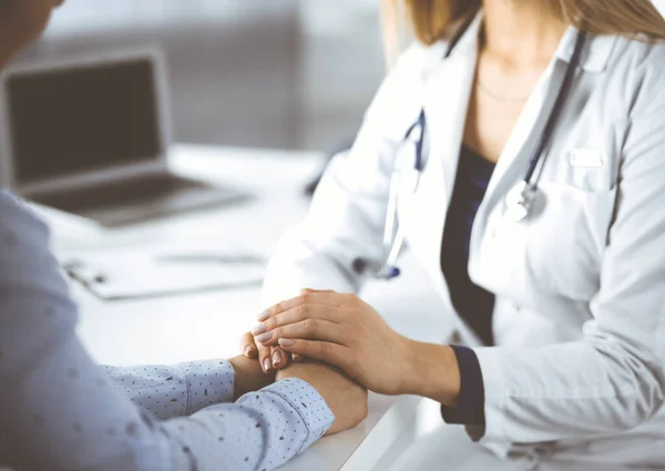 Bilinmeyen kadın-doktor, klinikteki dolapta otururken hastalarının ellerini tutuyor ve mevcut sağlık muayenesini tartışıyor. Steteskoplu bir doktor iş yerinde, yakın plan.