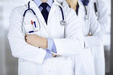 Hastane ofisinde çapraz kolları ve steteskopları olan bir grup modern doktor bir takım gibi duruyor. Doktorlar hastaları muayene etmeye ve yardım etmeye hazır. Tıbbi yardım, sağlık sigortası, en iyi hastalık