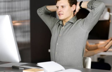 Yeşil tişörtlü kahverengi kıvırcık saçlı genç işadamı ve programcı, bilgisayar üzerinde sıkı çalıştıktan sonra ellerini uzatıyor ve kadın meslektaşıyla birlikte kabinede oturuyor. İş dünyası