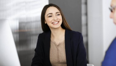 Genç ve güzel bir iş kadını, modern bir ofiste masada otururken iş arkadaşıyla konuşuyor. İş başarısı kavramı