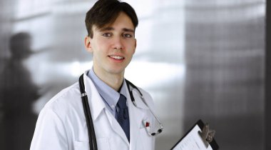 Modern klinikte dostane genç bir erkek doktor elinde bir panoyla dikiliyor. Bayan meslektaşım, doktorların arka planında ilaç kayıtları doldurmakla meşgul. Tıp konsepti