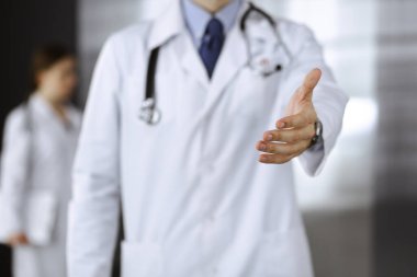 Bilinmeyen bir adam-doktor ayakta duruyor ve modern klinikte yardım eli uzatıyor. Kadın meslektaşının doktor geçmişinde acelesi var. Tıp konsepti