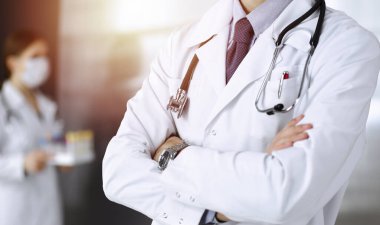 Güneşli klinikte kolları çapraz duran koruyucu maskeli kimliği belirsiz erkek doktor. Coronavirüs salgını sırasında ilaç kavramı