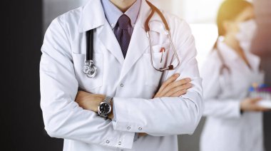 Güneşli klinikte kolları çapraz duran koruyucu maskeli kimliği belirsiz erkek doktor. Coronavirüs salgını sırasında ilaç kavramı