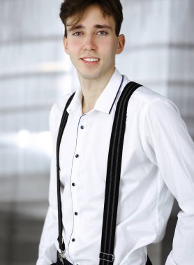 Modern ofiste beyaz gömlekli, dost canlısı genç bir işadamı duruyor.