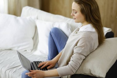 İş kadını, Covid-19 karantinası sırasında rahat oturma odasında dizüstü bilgisayarda çalışıyor. Coronavirus salgını sırasında evde konsept kal