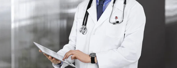 Unknown male doctor iusing tablet computer in his hands, while standing in clinic. Medicine concept during Coronavirus pandemic — Stock Photo, Image