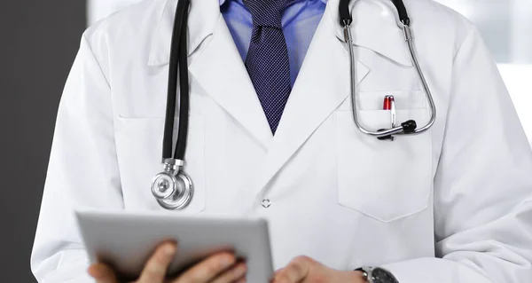 Unknown male doctor iusing tablet computer in his hands, while standing in clinic. Medicine concept during Coronavirus pandemic — Stock Photo, Image