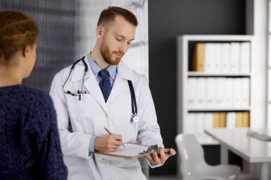 Dost canlısı kızıl sakallı doktor ve hasta kadın güneşli klinikte otururken sağlık muayenesini tartışıyorlar. Tıp konsepti